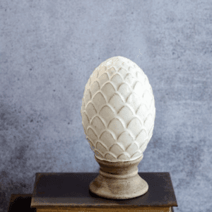 A white decorative egg sculpture on a pedestal against a gray backdrop.